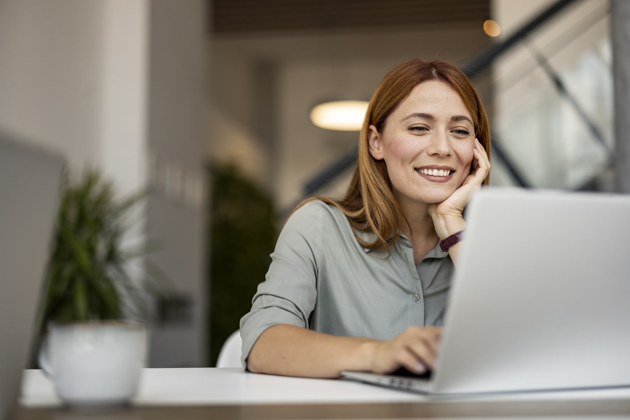 Happy woman sitting at her desk, working on a laptop