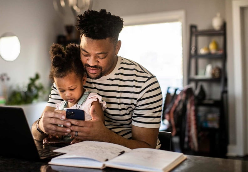 Father working from a table with child in his lap.